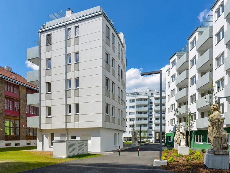 Photo: several modern residential buildings around a tarmac footpath, surrounded by stone sculptures and green lawns