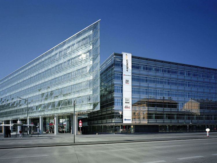 Photo: office building with a tapered glass façade; in front of it a multi-lane road